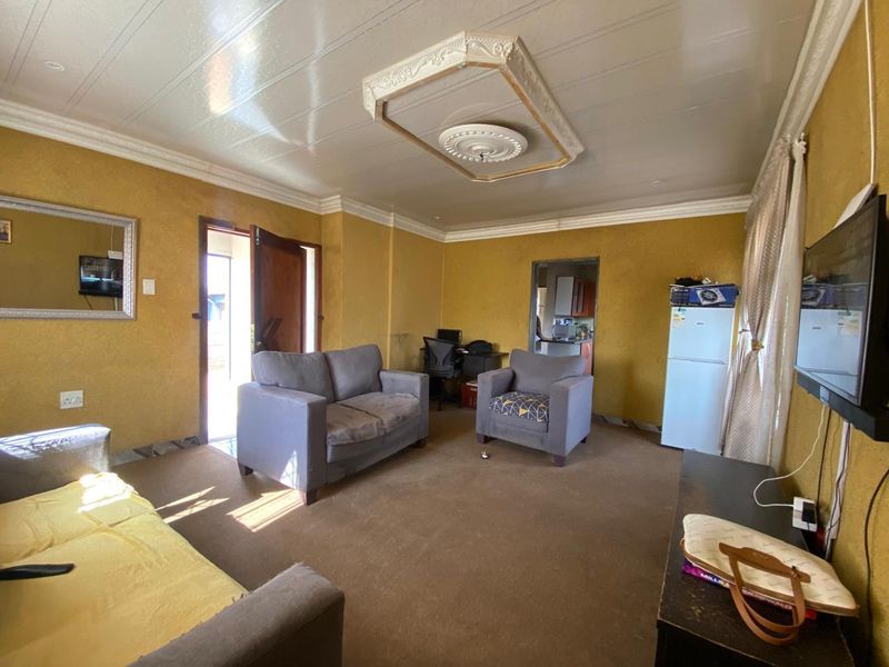 A living room featuring textured walls, a decorative ceiling rose with coving, and carpeted flooring, providing a dated but functional living space.
