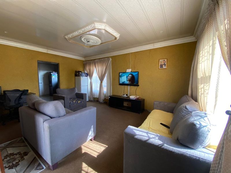 A living room featuring a textured ceiling with a decorative ceiling rose and coving, providing a functional space with potential for cosmetic updates.