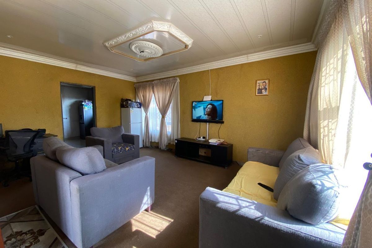 A living room featuring a textured ceiling with a decorative ceiling rose and coving, providing a functional space with potential for cosmetic updates.