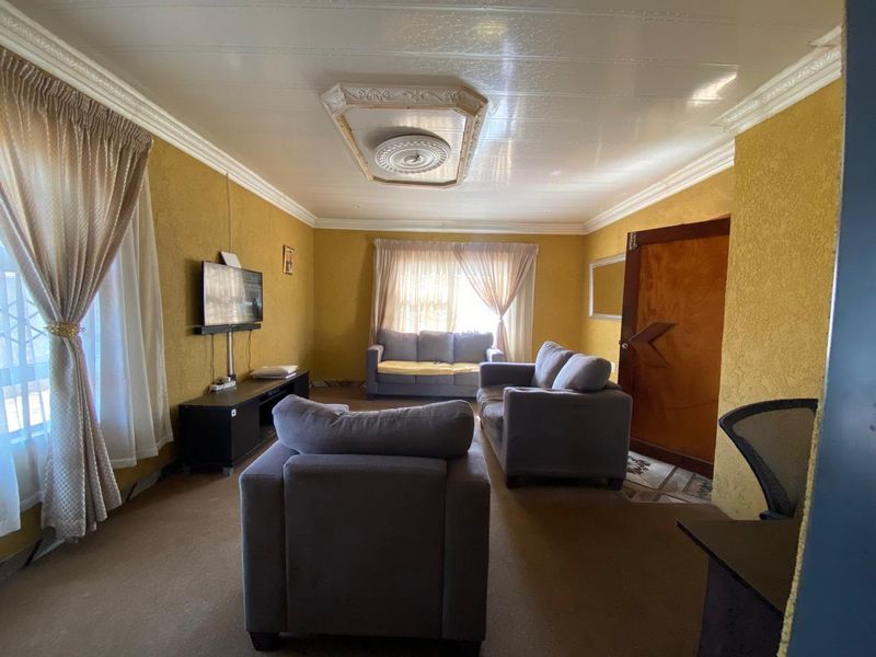 A living room featuring textured walls, decorative ceiling detailing, and coved cornicing, offering a dated aesthetic ready for modernization.