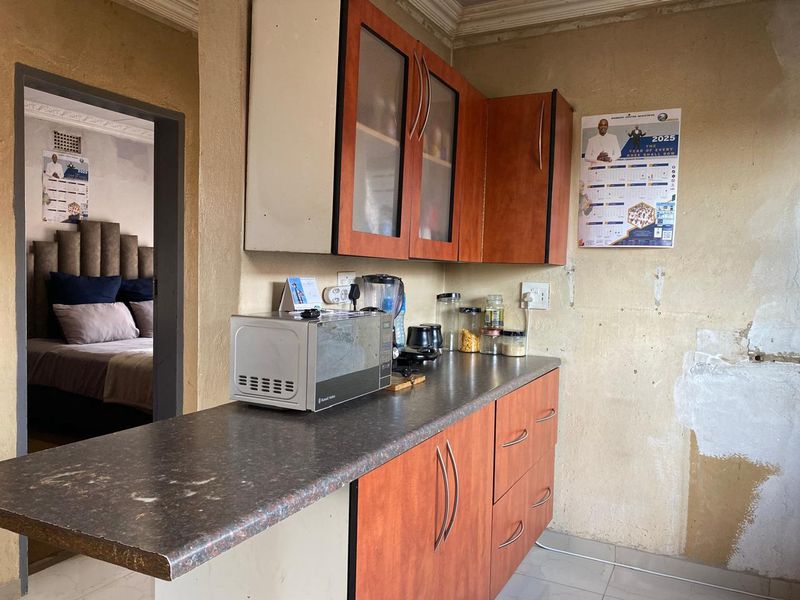 A compact kitchen area featuring wood-look cabinetry and laminate countertops, requiring wall repairs and cosmetic updates to improve the overall finish.