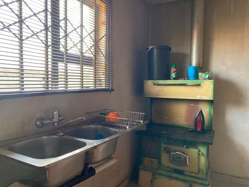 A dated kitchen area featuring a double stainless steel sink, wall-mounted tap, and a vintage solid fuel stove with visible wear to finishes.
