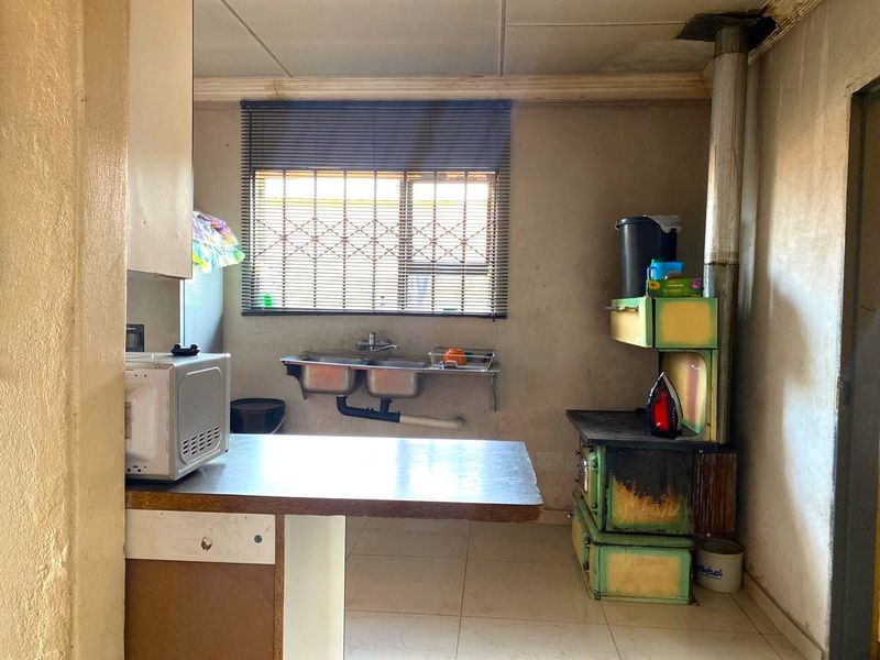 A dated kitchen featuring a double stainless steel sink, tiled flooring, and a built-in wood-burning stove, requiring significant cosmetic updates and repairs.