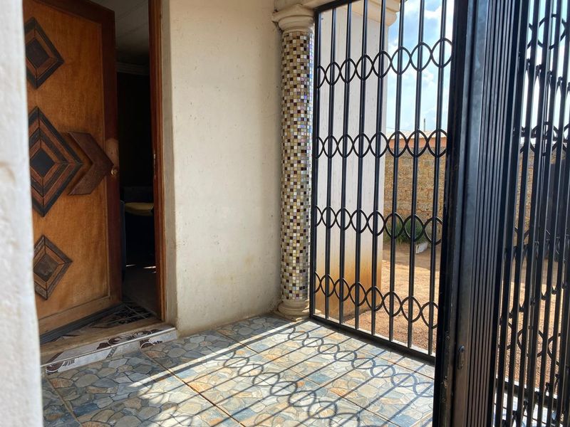 Covered entrance patio featuring decorative mosaic tiled column, patterned floor tiles, and a secure metal gate.