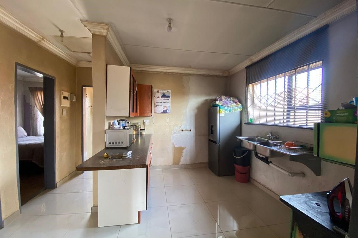 A functional kitchen space featuring tiled flooring, a double bowl sink, and built-in cabinetry, currently requiring cosmetic updates and wall repairs.