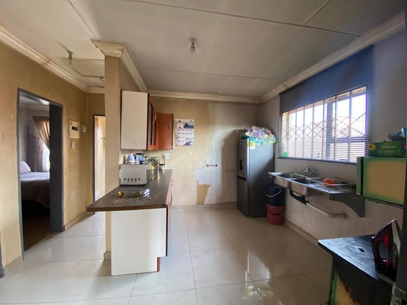 A functional kitchen space featuring tiled flooring, a double bowl sink, and built-in cabinetry, currently requiring cosmetic updates and wall repairs.