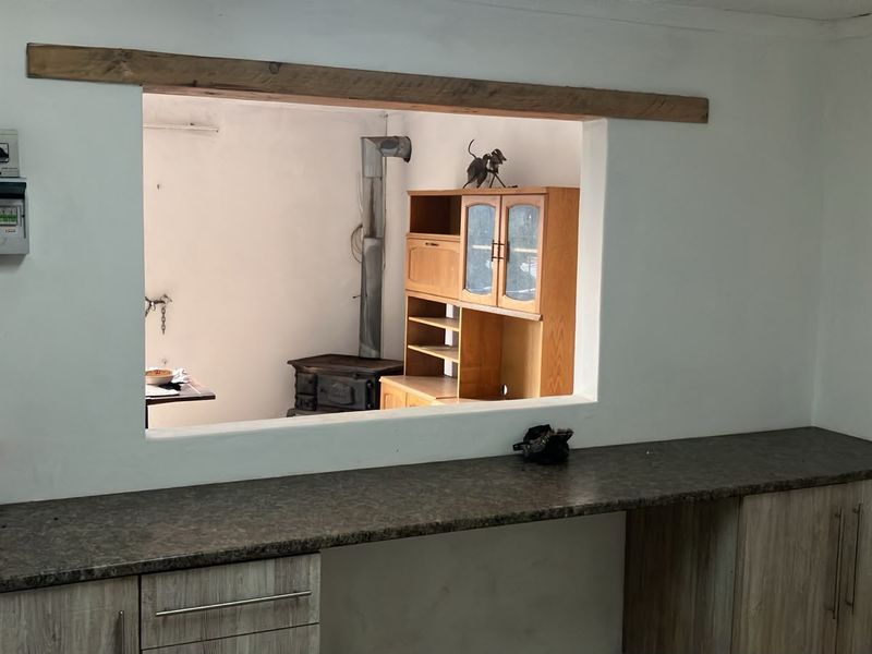 Kitchen area featuring a pass-through window with a timber lintel, laminate countertops, and built-in cabinetry, requiring some finishing touches to the wall surfaces.