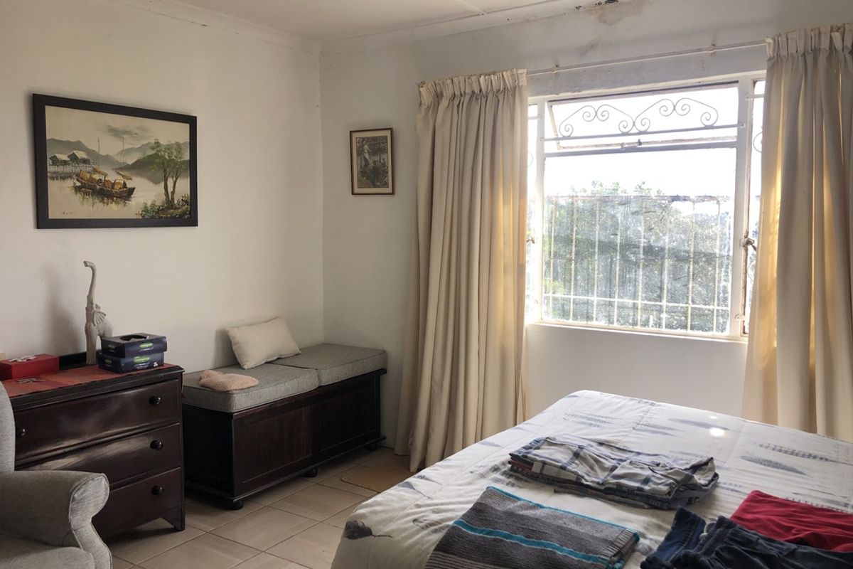 A bedroom featuring tiled flooring and a window with security bars. Visible water staining on the ceiling indicates potential maintenance requirements.