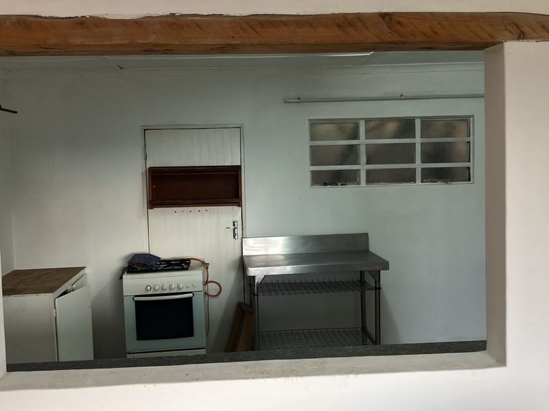 A basic kitchen area featuring a freestanding stove, stainless steel prep station, and a timber lintel, offering a functional space ready for modernization.