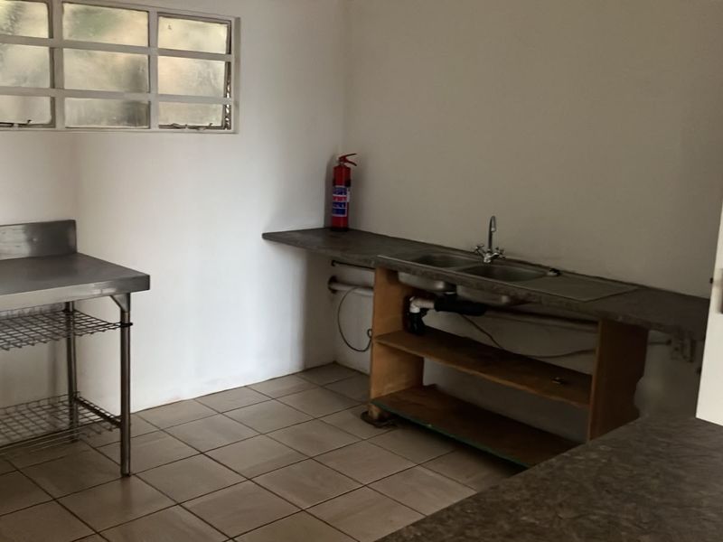 A functional scullery or utility area featuring a double bowl sink, stainless steel prep table, and tiled flooring, ready for renovation or custom cabinetry.