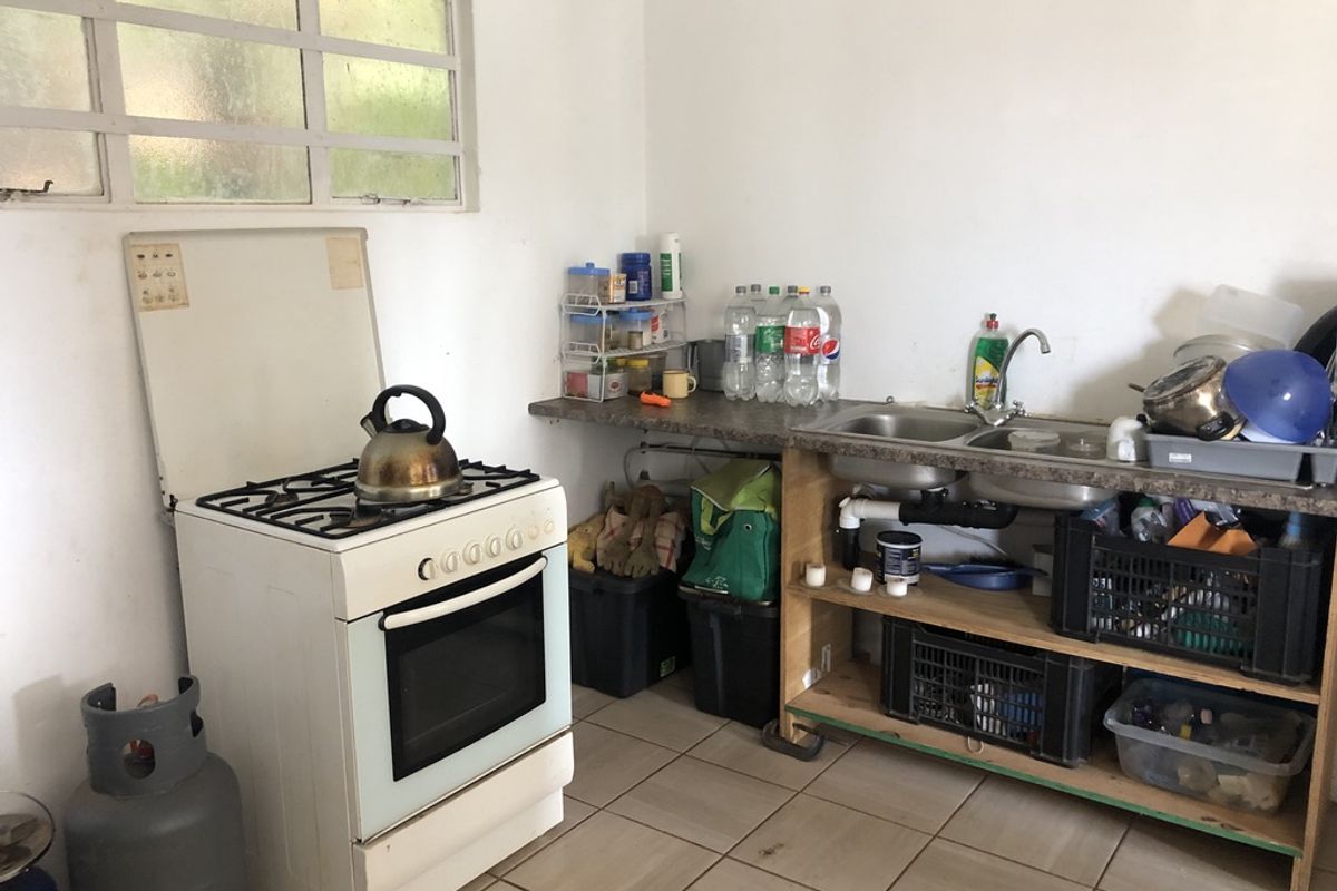 A functional kitchen area featuring a gas stove, double bowl sink, and open shelving with tiled flooring.