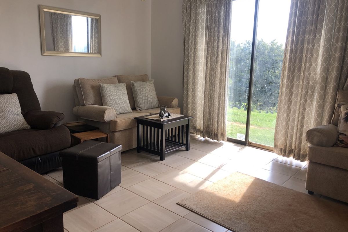 A living room featuring tiled flooring and a large sliding glass door providing natural light and access to the garden.