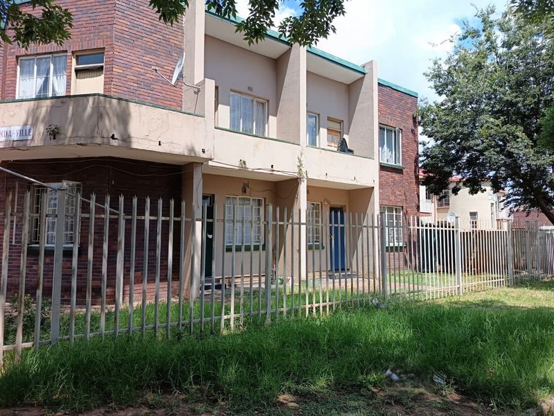 Front elevation of a multi-story apartment complex featuring face brick and plaster finishes, with a secure perimeter fence and balcony access.