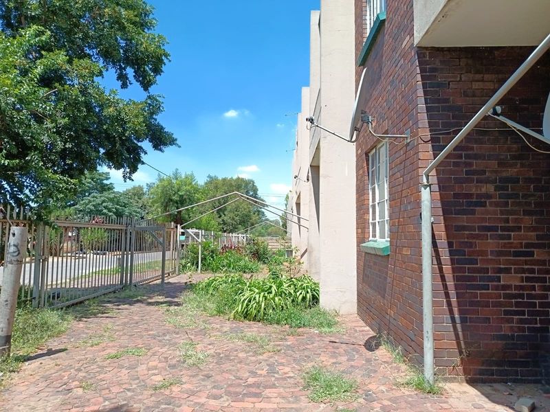 Exterior view of the apartment building featuring a brick facade, paved walkway, and metal security fencing along the perimeter.