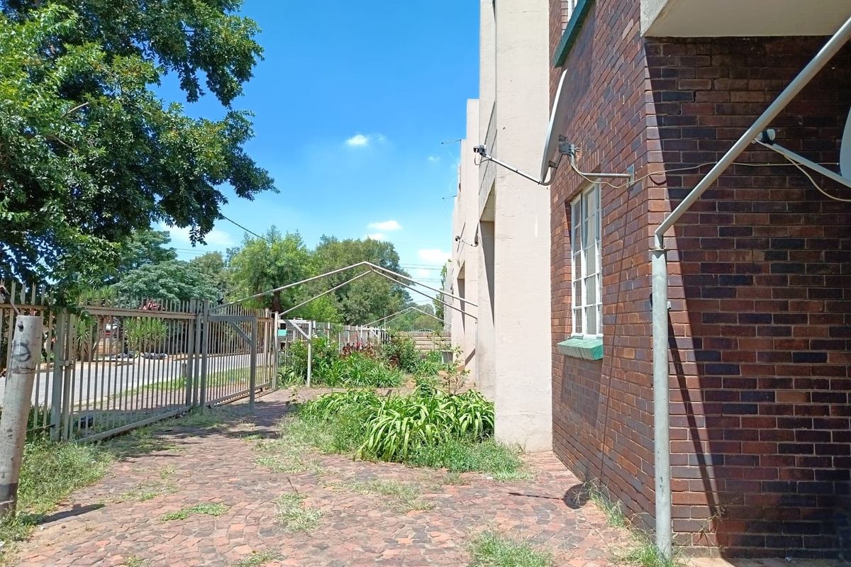 Exterior view of the apartment building featuring a brick facade, paved walkway, and metal security fencing along the perimeter.