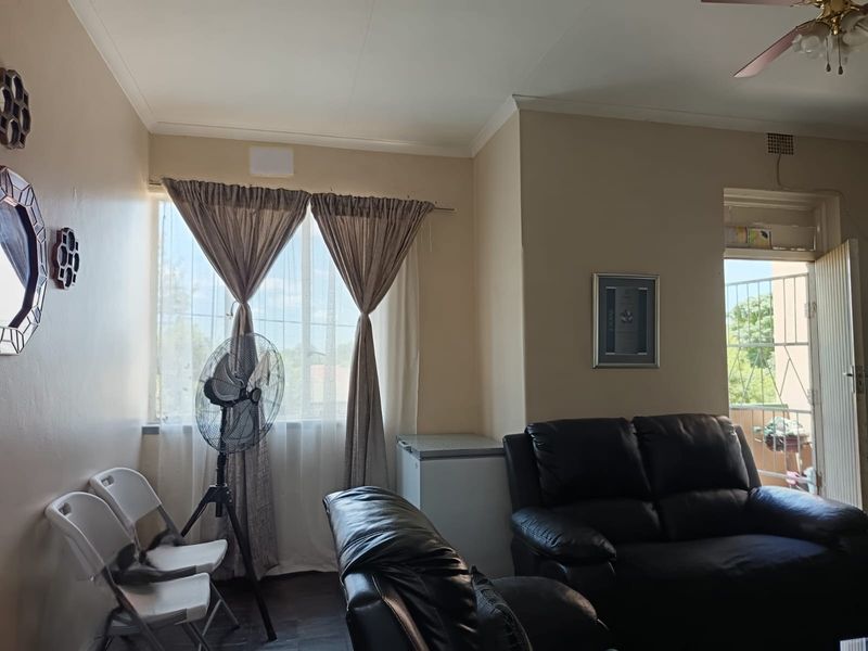 A living room area featuring a ceiling fan, neutral wall tones, and access to an outdoor balcony through a security gate.