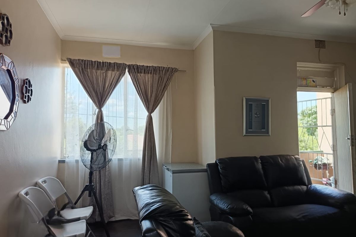 A living room area featuring a ceiling fan, neutral wall tones, and access to an outdoor balcony through a security gate.