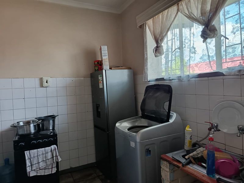 A functional kitchen area featuring a tiled splashback, stainless steel sink, and window with security bars, requiring some cosmetic updates to finishes.