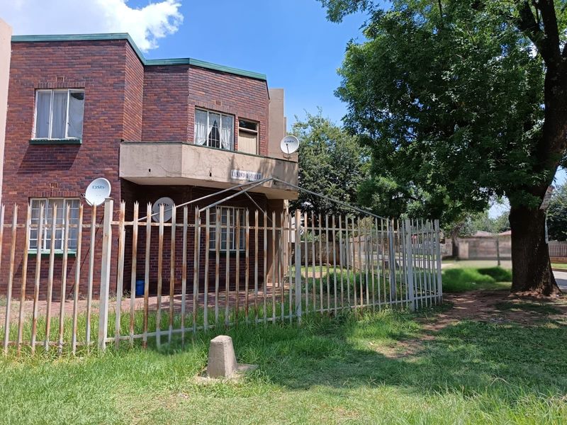 Front exterior view of a face brick apartment building featuring a balcony and metal security fencing.