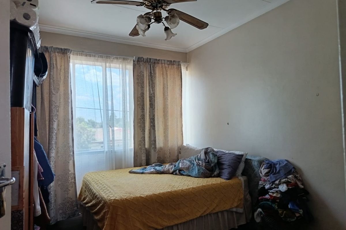 A functional bedroom featuring a ceiling fan and natural light through a window with curtains.