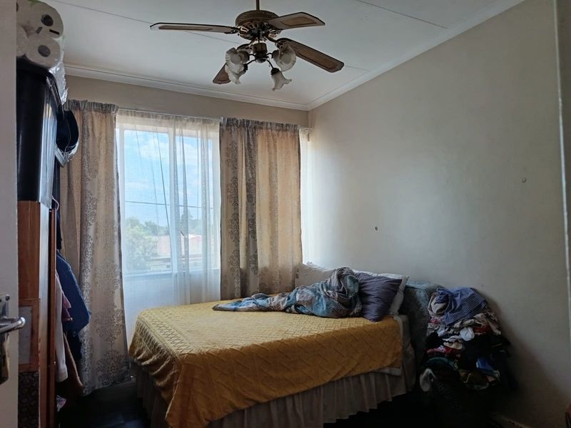 A functional bedroom featuring a ceiling fan and natural light through a window with curtains.