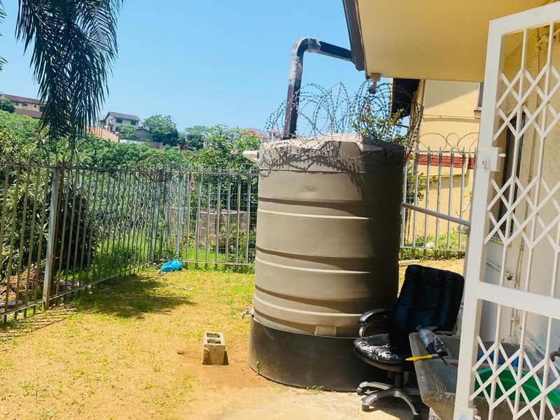 Rear exterior area featuring a large water storage tank, security fencing with razor wire, and a metal security gate.