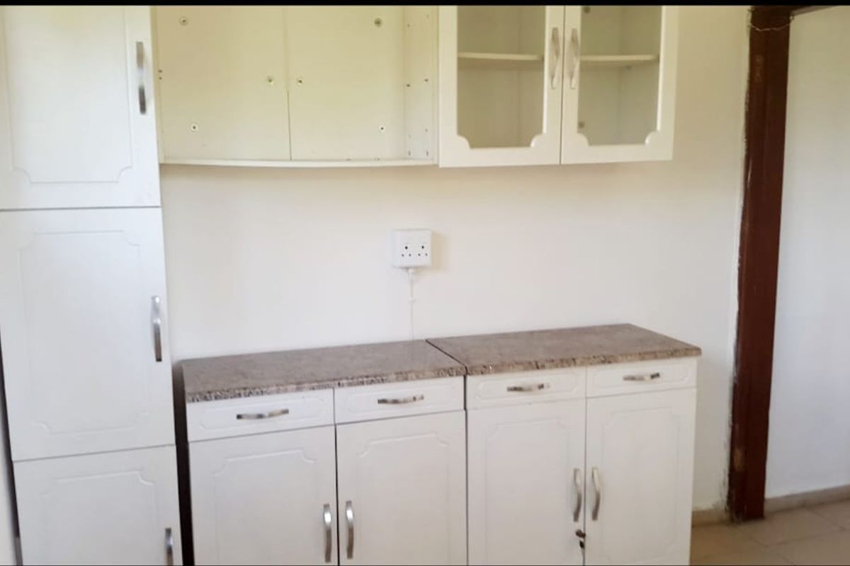 A compact kitchen area featuring white built-in cabinetry, stone-look countertops, and glass-fronted wall units, currently in need of minor repairs and updates.