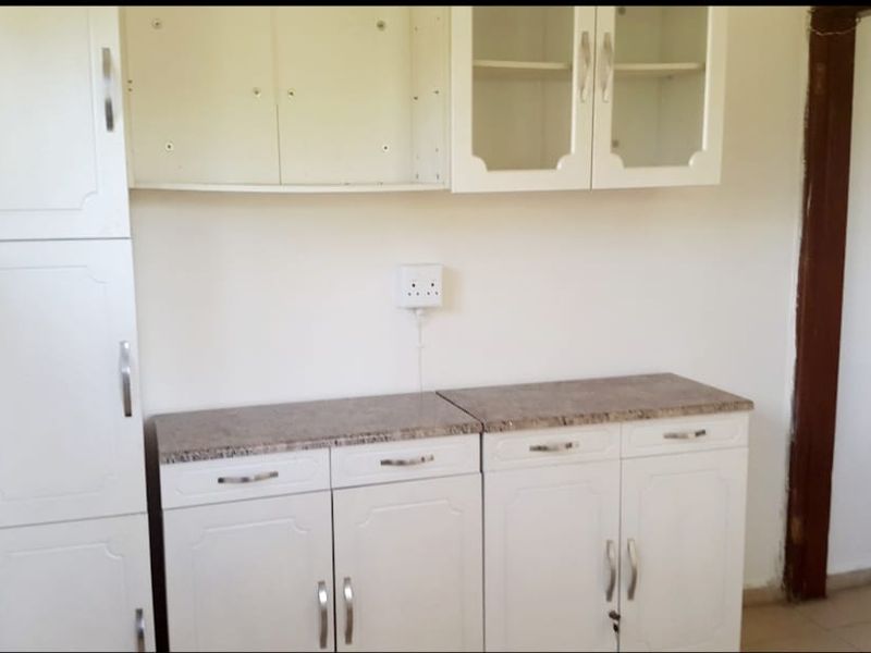 A compact kitchen area featuring white built-in cabinetry, stone-look countertops, and glass-fronted wall units, currently in need of minor repairs and updates.