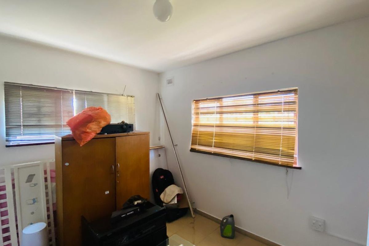 A bedroom featuring tiled flooring and dual windows with fitted venetian blinds, offering a blank canvas for potential interior updates.