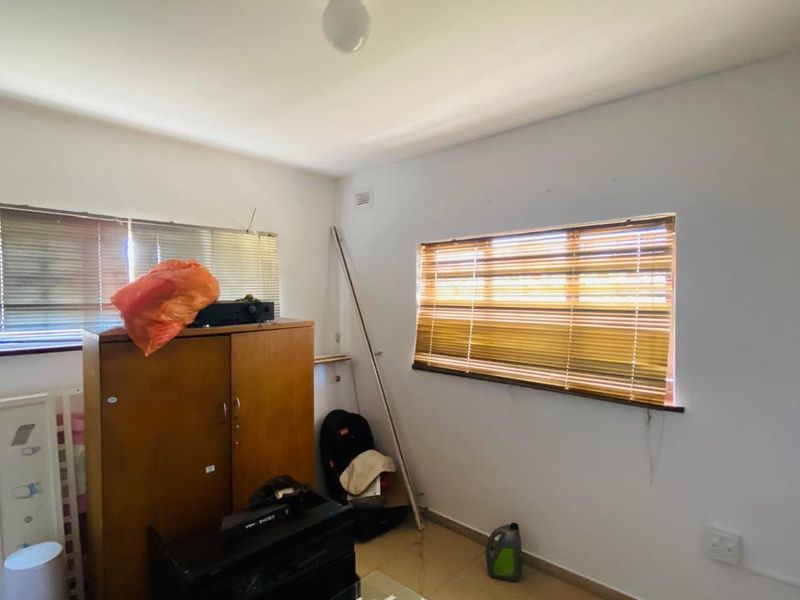 A bedroom featuring tiled flooring and dual windows with fitted venetian blinds, offering a blank canvas for potential interior updates.
