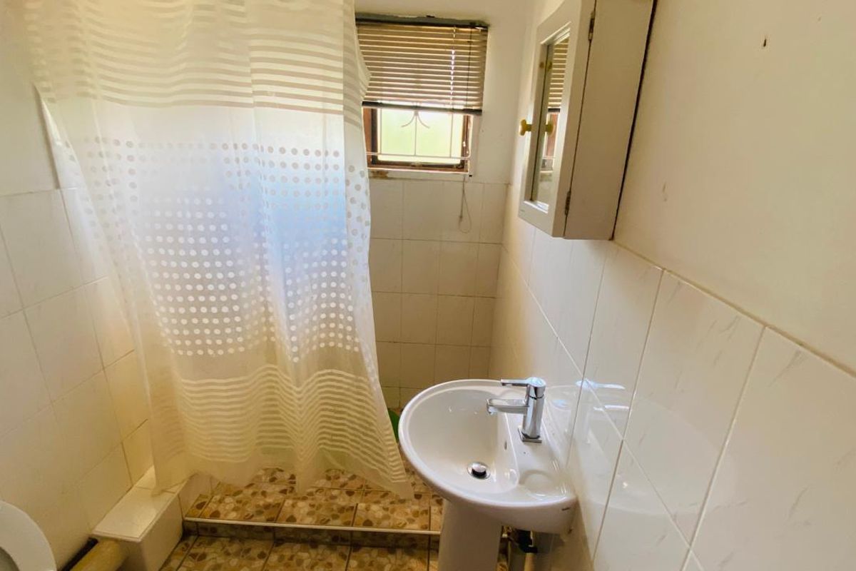 A compact bathroom featuring a pedestal sink, wall-mounted medicine cabinet, and a shower area with tiled walls and a window.