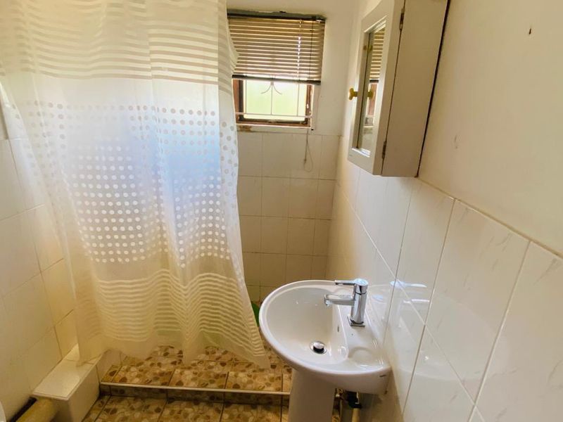 A compact bathroom featuring a pedestal sink, wall-mounted medicine cabinet, and a shower area with tiled walls and a window.
