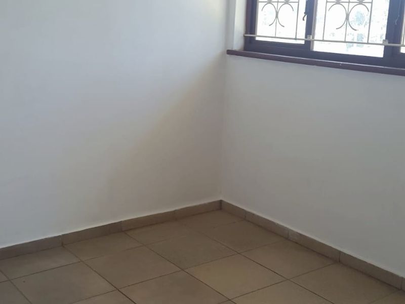 An empty bedroom featuring neutral tiled flooring and a window fitted with security bars, offering a blank canvas for personalization.