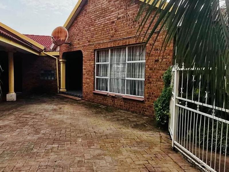 Front exterior view of a face brick house featuring a paved driveway, covered patio area, and secure metal gate entrance.