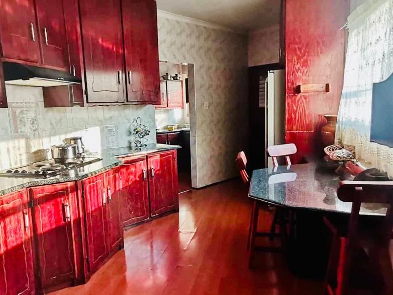A dated kitchen featuring dark wood cabinetry, granite countertops, built-in oven, and hob, with a small breakfast nook area.