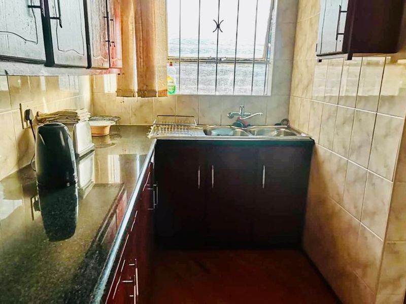 A compact kitchen featuring dark wood cabinetry, granite countertops, a double sink, and tiled splashbacks with a window providing natural light.