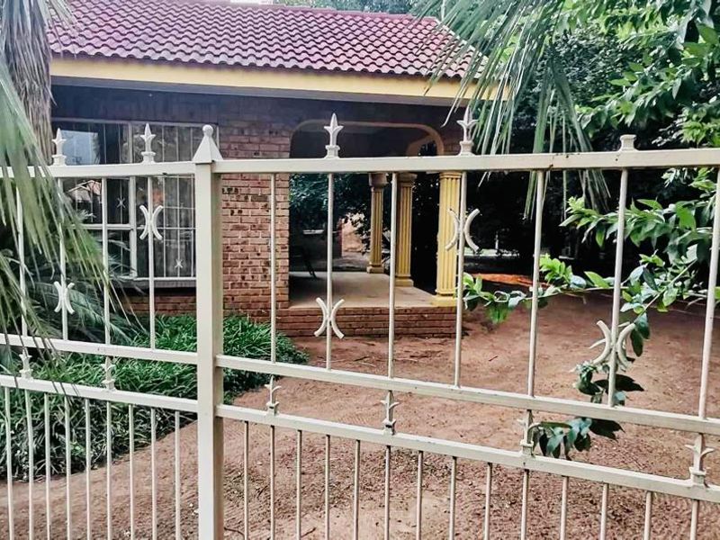 Front view of a face brick house featuring a covered porch, tiled roof, and decorative metal perimeter fencing.