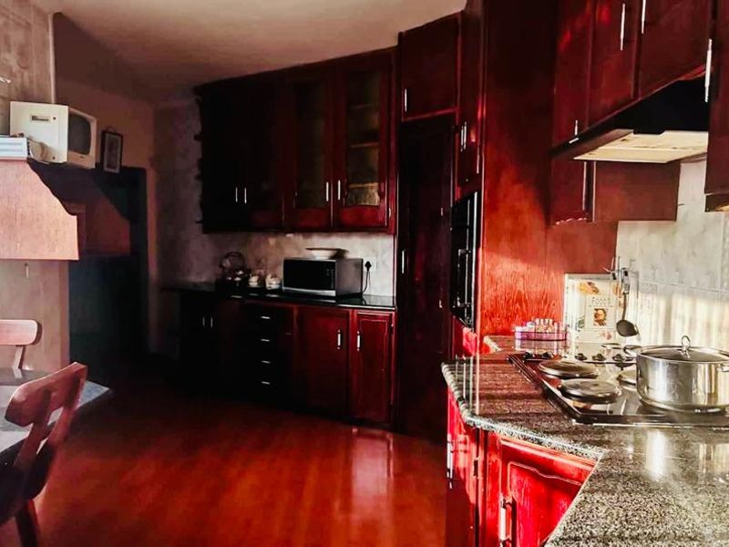 A functional kitchen featuring dark wood cabinetry, granite countertops, a gas hob with extractor fan, and tiled backsplash.
