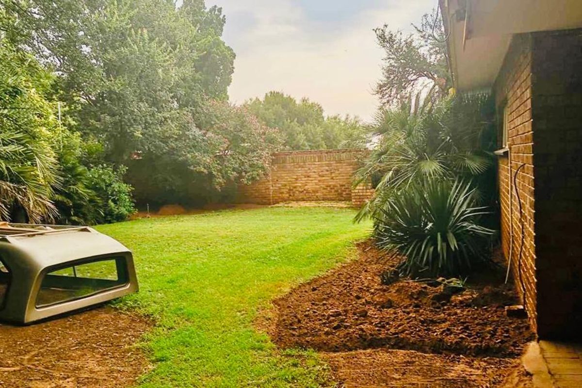 A rear garden view featuring a lawn, mature trees, and a brick boundary wall adjacent to the house's brick exterior.