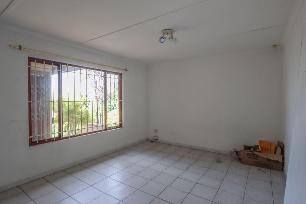 A vacant bedroom featuring tiled flooring, a large window with security bars, and neutral white walls, offering a blank canvas for personalization.