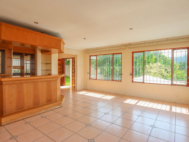 Spacious room featuring a built-in wooden bar, tiled flooring, and large windows with security bars, offering a functional space for entertainment.