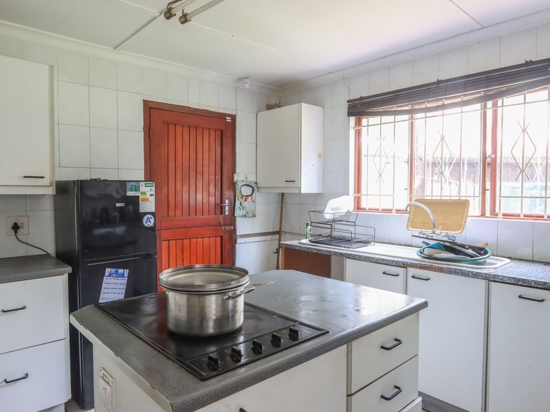 A functional kitchen featuring built-in cabinetry, laminate countertops, a central hob, and tiled splashbacks, offering potential for modernization and cosmetic updates.