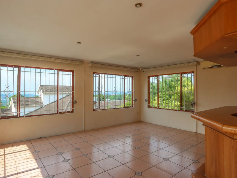 Spacious living area featuring tiled flooring, built-in wooden bar counter, and large windows with security bars offering natural light and views.
