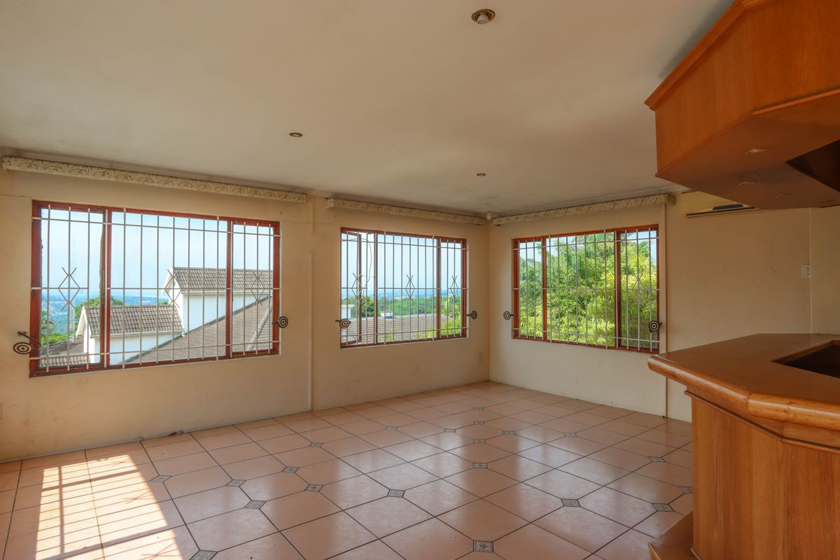 Spacious living area featuring tiled flooring, built-in wooden bar counter, and large windows with security bars offering natural light and views.