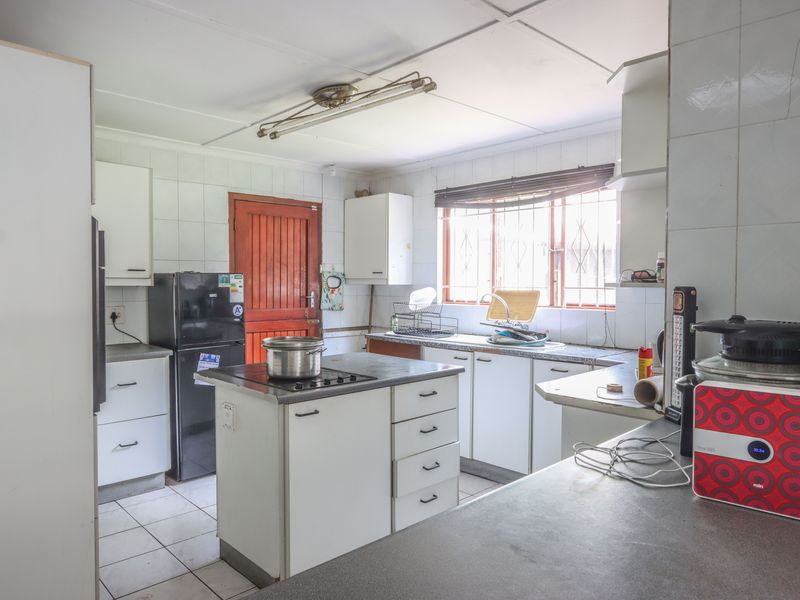 A functional kitchen featuring built-in cabinetry, a central island with a hob, tiled splashbacks, and a double sink, offering potential for modernization.