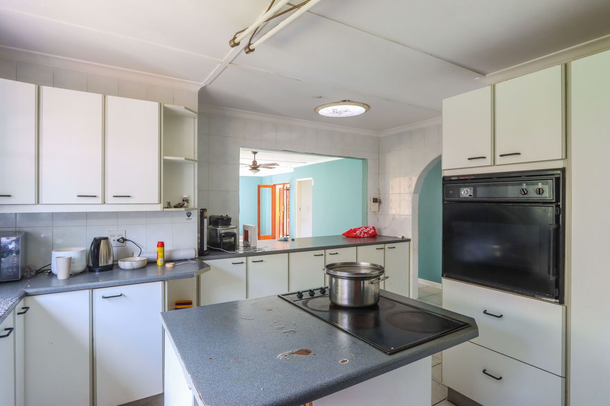 A functional kitchen featuring white cabinetry, laminate countertops, a built-in oven, and an electric cooktop, with an open-plan layout connecting to adjacent living areas.