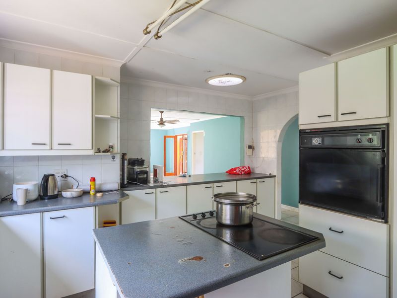 A functional kitchen featuring white cabinetry, laminate countertops, a built-in oven, and an electric cooktop, with an open-plan layout connecting to adjacent living areas.