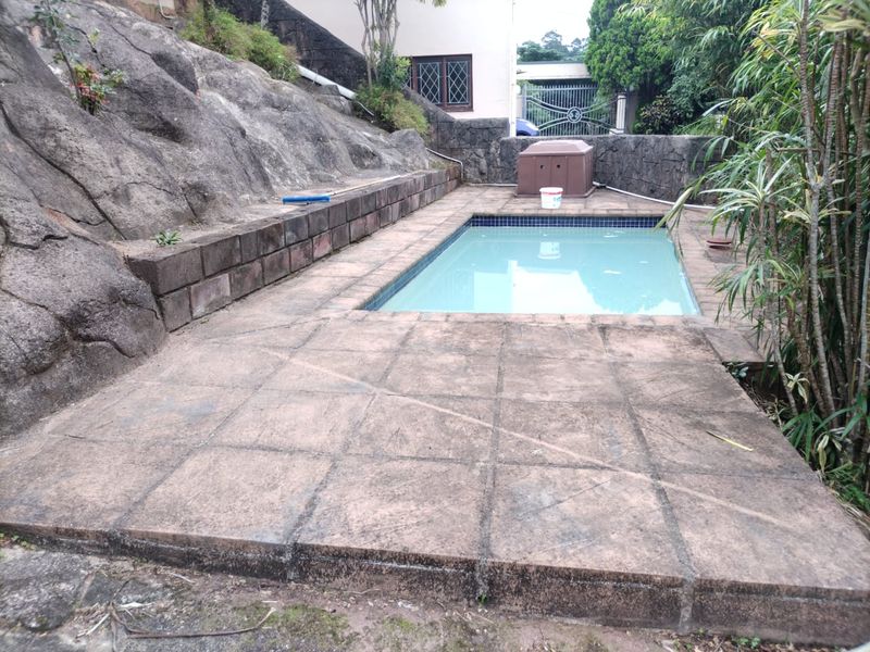 Outdoor pool area featuring a paved deck, integrated rock face retaining walls, and established garden surroundings.