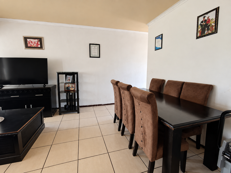A spacious living and dining area featuring neutral wall finishes, ceramic floor tiles, and decorative ceiling cornicing.