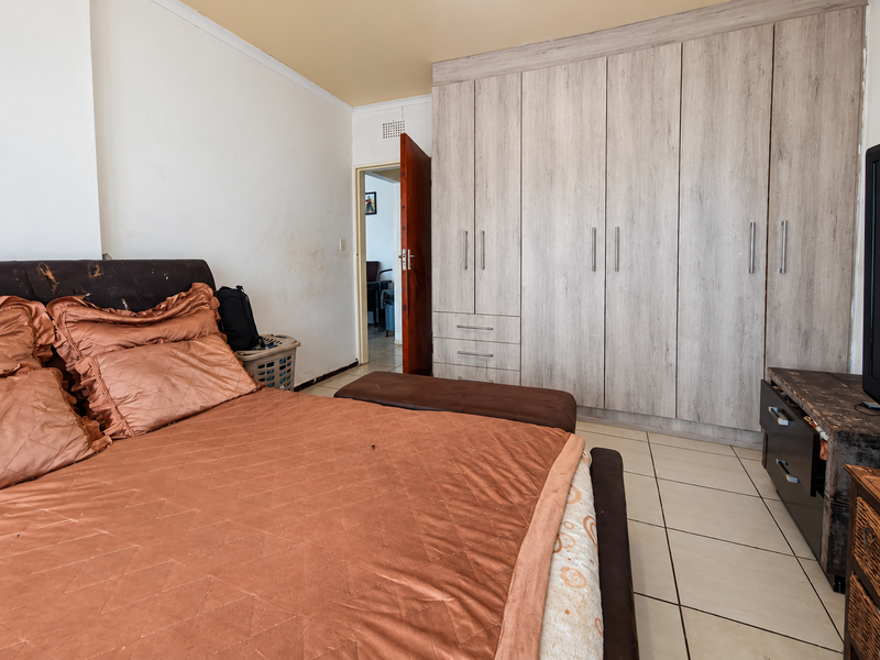 A bedroom featuring light wood-finish built-in cupboards and tiled flooring, with access to an adjacent room through a wooden door.